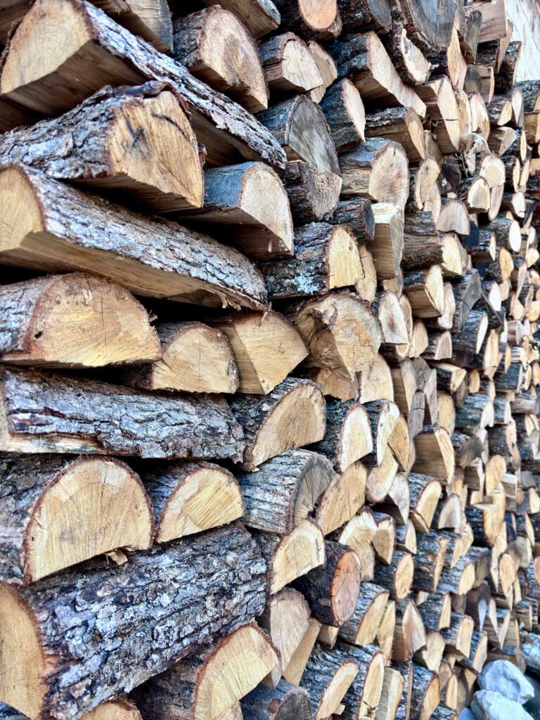Pile dense de bois de chauffage fendu, bûches empilées révélant les textures d'écorce rugueuse et les couleurs du bois coupé.